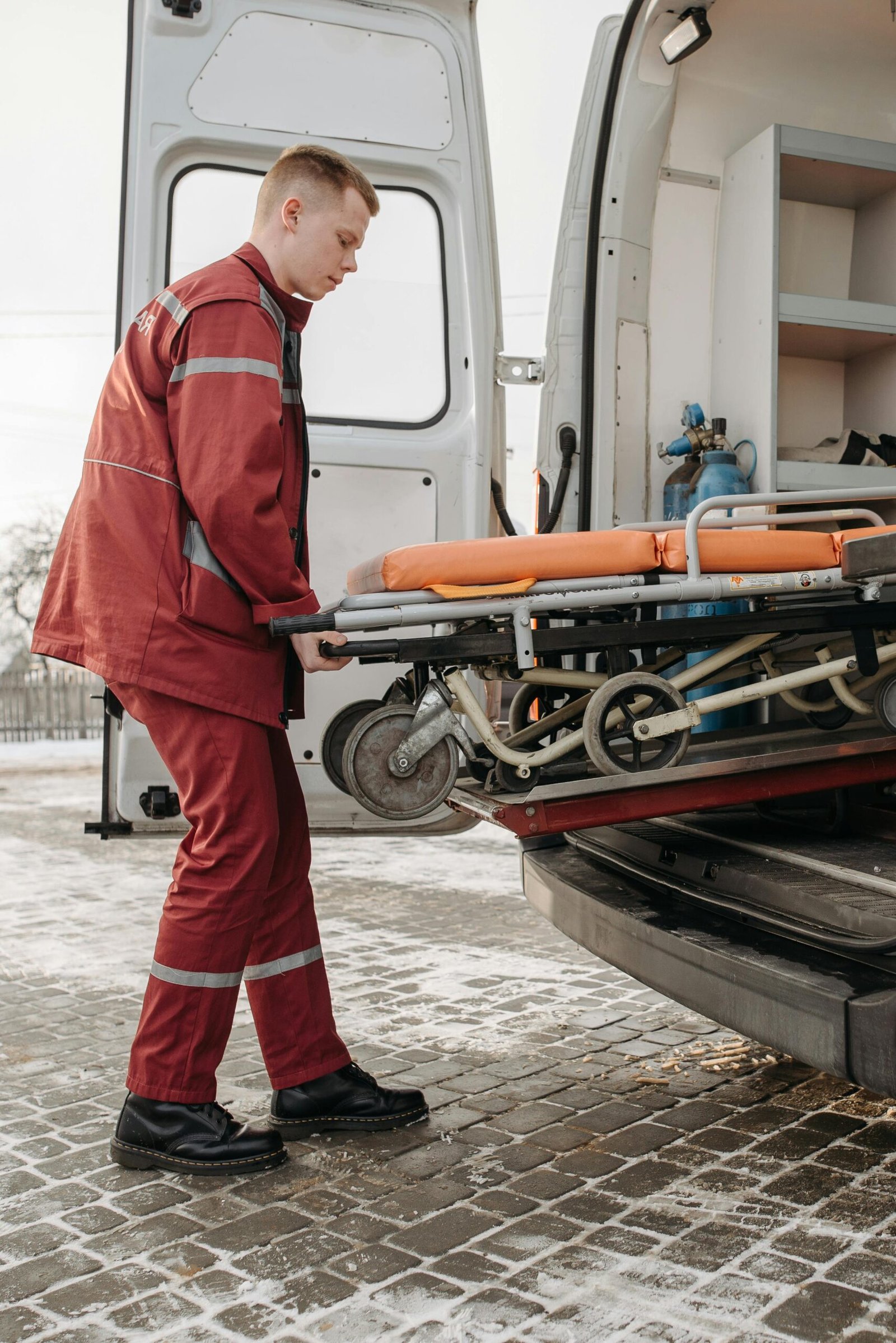 A paramedic loads a stretcher into an ambulance outdoors during the day.