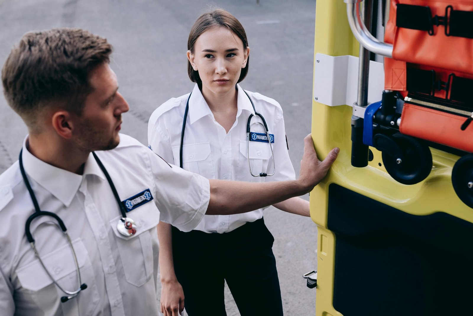 Two paramedics in uniform prepare an ambulance for emergency response, demonstrating teamwork.